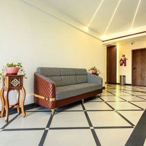 A room with a sofa, a small wooden table with a plant, and a tiled floor.