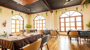 A dining area with tables set for service, large windows with arched tops, and hanging plants.