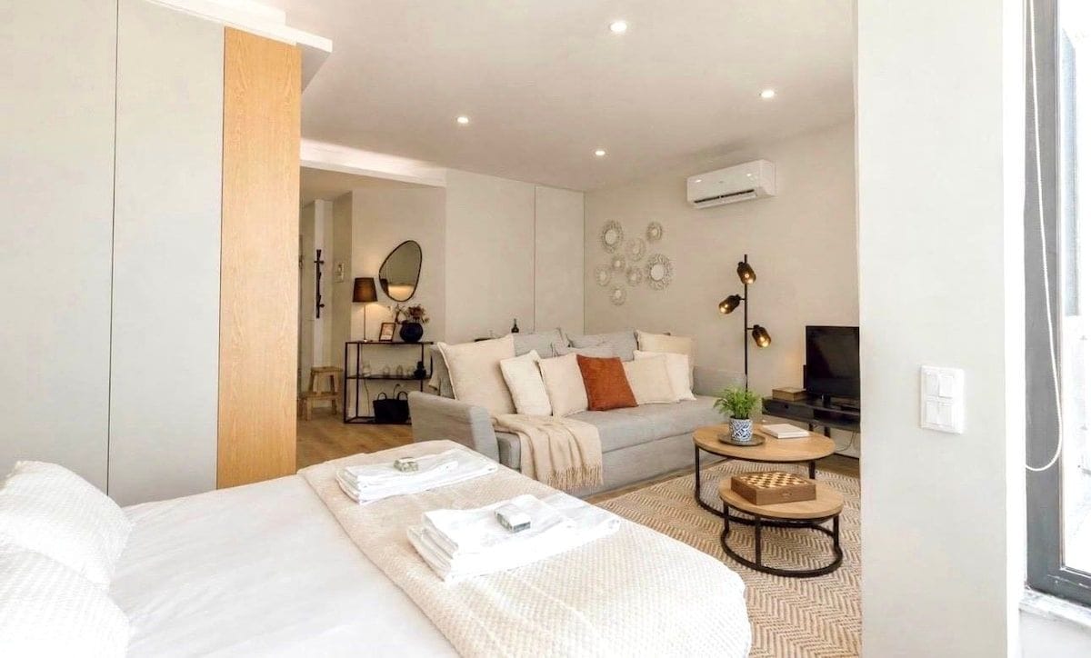 A modern hotel room with a bed, a sofa, a small table, and a TV.