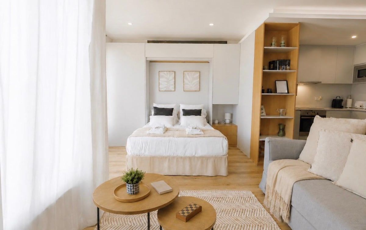 A modern bedroom with a large bed, bedside tables, and a view into a kitchen area.
