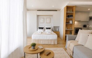 Ein modernes Schlafzimmer mit einem großen Bett, Nachttischen und Blick in einen Küchenbereich.
