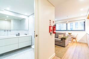 A modern interior with a bathroom, a sofa, a small table, and a window. - The Braamcamp Collection Apt A (Porto)