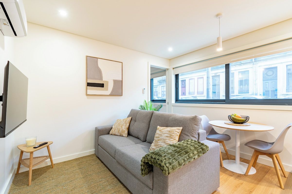 A modern living room with a grey sofa, a small round table, and a TV on a stand.