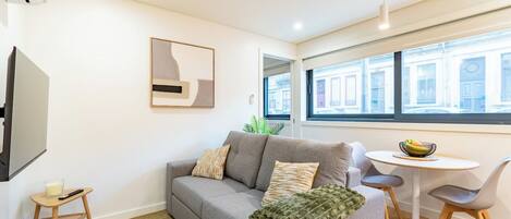 A modern living room with a grey sofa, a small round table, and a TV on a stand.