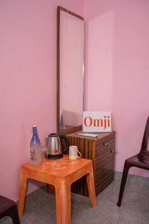 Una habitación con una pared rosa, un aparador de madera, un espejo, una mesita con un hervidor, una taza y una botella.
