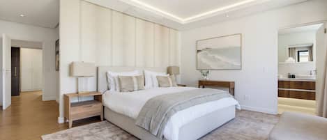 A modern bedroom with a large bed, bedside tables, a nightstand, a mirror, and a view of the bathroom.