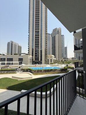 A high-rise building with a pool and a well-maintained lawn. - 1-BHK - Dubai Creek Harbor - Pool View (Dubai)