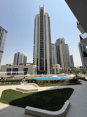 Un immeuble de grande hauteur au design moderne, entouré d’autres bâtiments imposants, d’une piscine et d’un espace paysager agrémenté de pelouses et de sentiers.