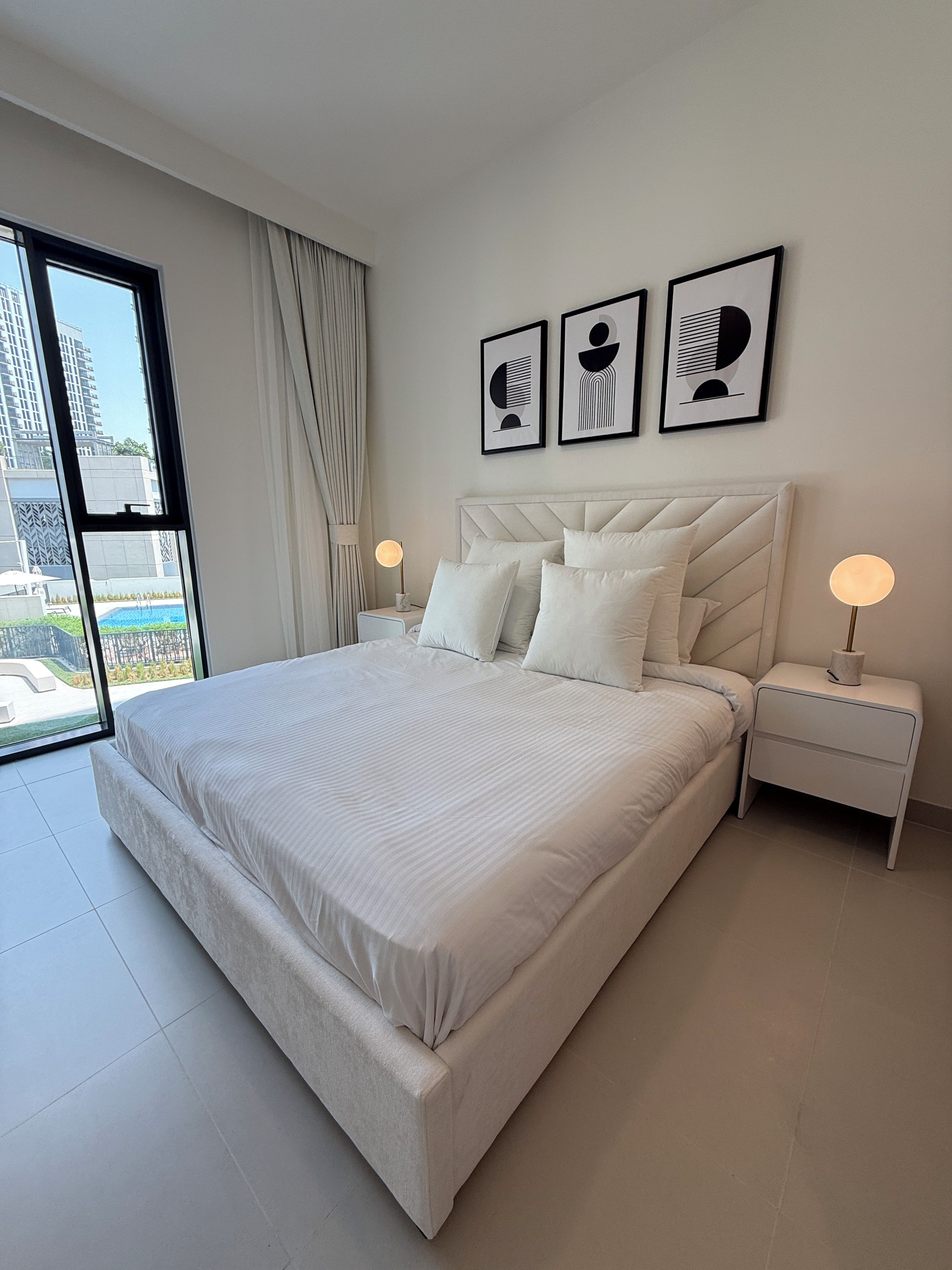 Een moderne slaapkamer met een groot bed, twee nachtkastjes en uitzicht op een gebouw door een raam.