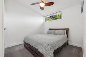 Ein Schlafzimmer mit einem Bett, einem Deckenventilator, einem Fenster und einer Tür.