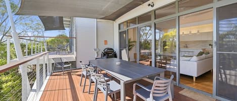 A covered outdoor dining area with a table and chairs, a grill, and a view of the interior.