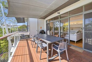 A covered outdoor dining area with a table and chairs, a grill, and a view of the interior. - Paradise Palms | Walk to Beach | Boat Parking (Agnes Water)