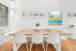 A modern dining area with a wooden table, white chairs, and a potted plant. - Paradise Palms | Walk to Beach | Boat Parking (Agnes Water)