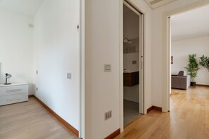A hallway with a wooden floor, white walls, and a door leading to another room. - GuestHost - Bright Apartment with a Balcony near the MM3 (Milan)