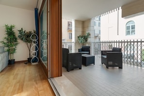 A balcony with wicker furniture, potted plants, and a view of neighboring buildings. - GuestHost - Bright Apartment with a Balcony near the MM3 (Milan)