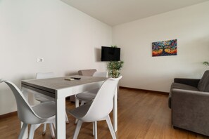 A modern living room with a dining area, a flat-screen TV mounted on the wall, and a colorful painting. - GuestHost - Bright Apartment with a Balcony near the MM3 (Milan)