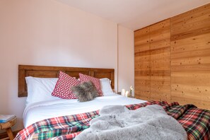 A bedroom with a wooden headboard, white bedding, a plaid blanket, and a fluffy gray throw.