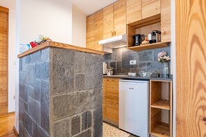 A kitchen with a stone accent wall, wooden cabinets, a white dishwasher, and a built-in shelf with kitchen items.