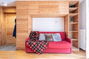 Ein rotes Sofa mit einer karierten Decke und zwei Kissen, platziert an einer Holzwand mit einer Tafel darüber.