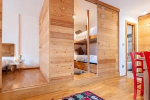 Ein Zimmer mit einem Holzschrank, einem Etagenbett, einem roten Stuhl und einem gemusterten Teppich.