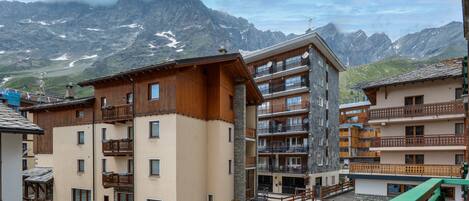 A mountain resort with multi-story buildings, balconies, and a view of snow-capped peaks.