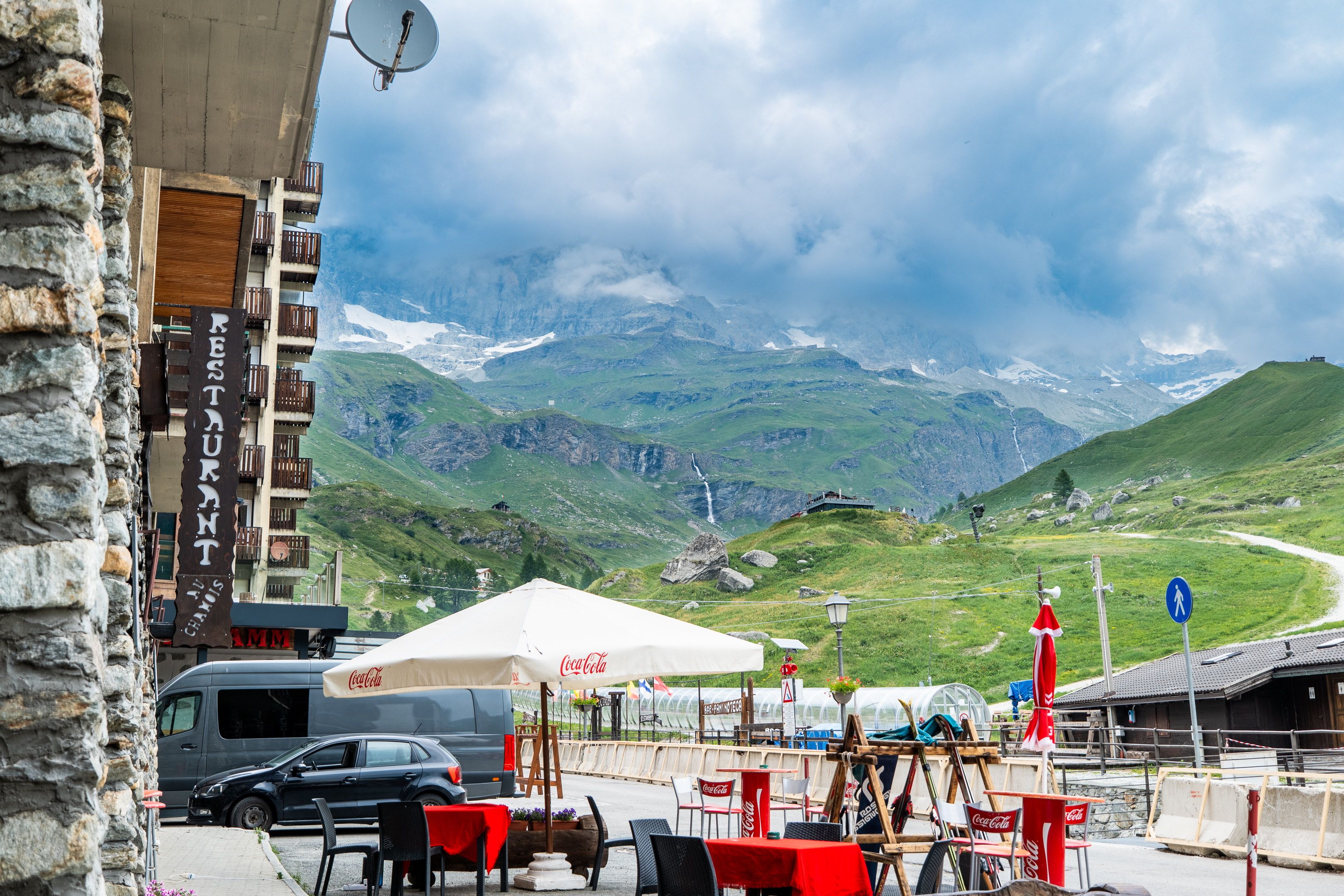 A restaurant with outdoor seating, a mountain view, and a sign for 'RESTAURANT CHEMUS'.