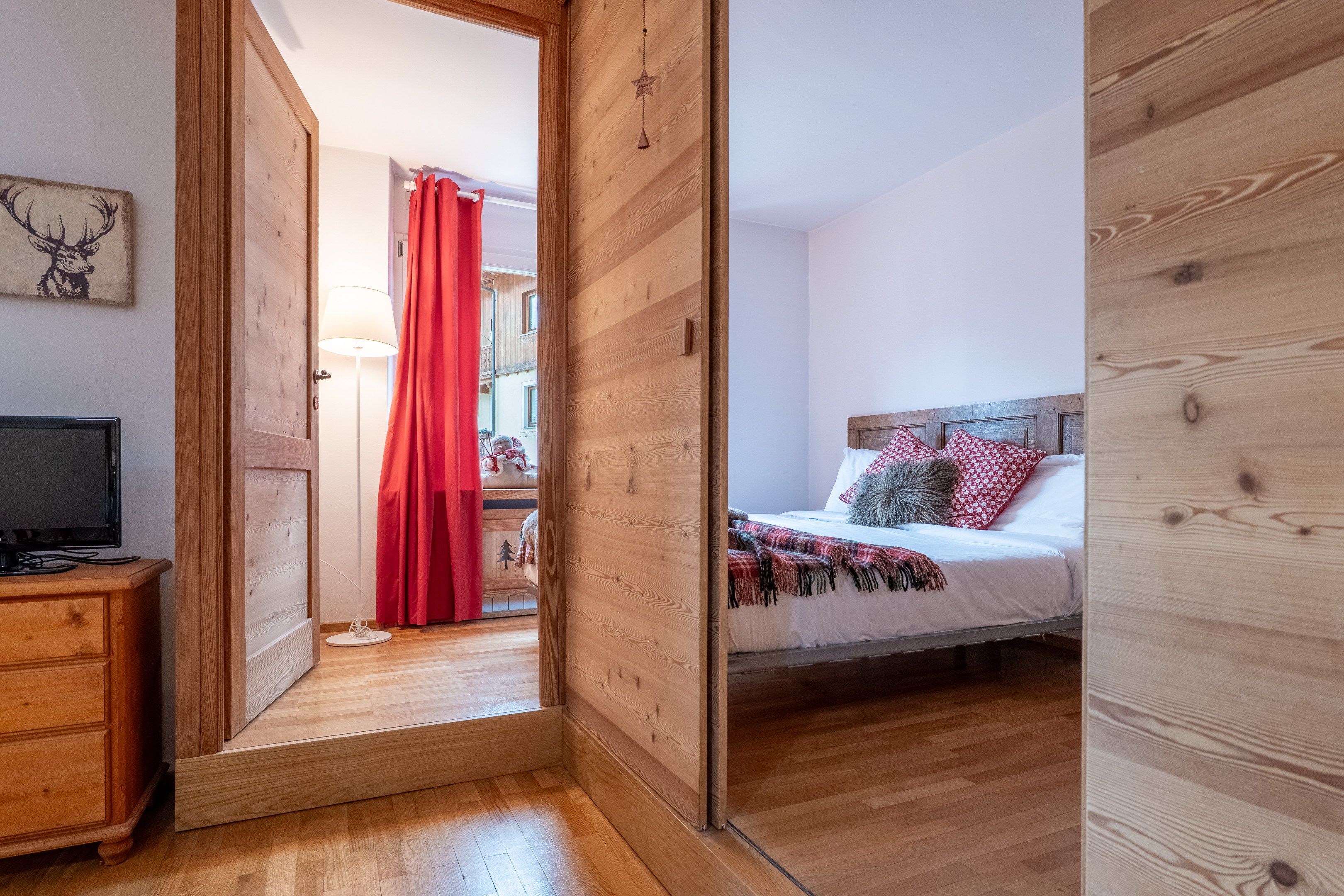 A bedroom with a wooden floor, a bed with patterned bedding, a bedside table, and a television on a wooden dresser.