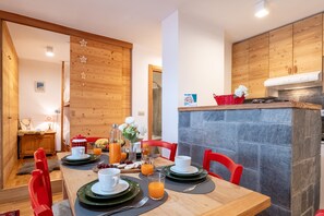 A dining area with a wooden table, red chairs, and a stone wall.