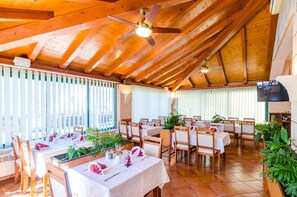 Ein Restaurant mit Holzbalken, weißen Tischdecken und grünen Pflanzen.
