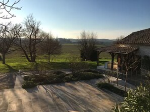 A stone patio leading to a covered outdoor area with a view of a green field and trees. - Countryside lodge (Saint-Eutrope-de-Born)
