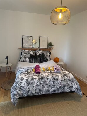 A bedroom with a bed, a hanging light fixture, a small table, and a wall-mounted shelf with decorative items. - Countryside lodge (Saint-Eutrope-de-Born)