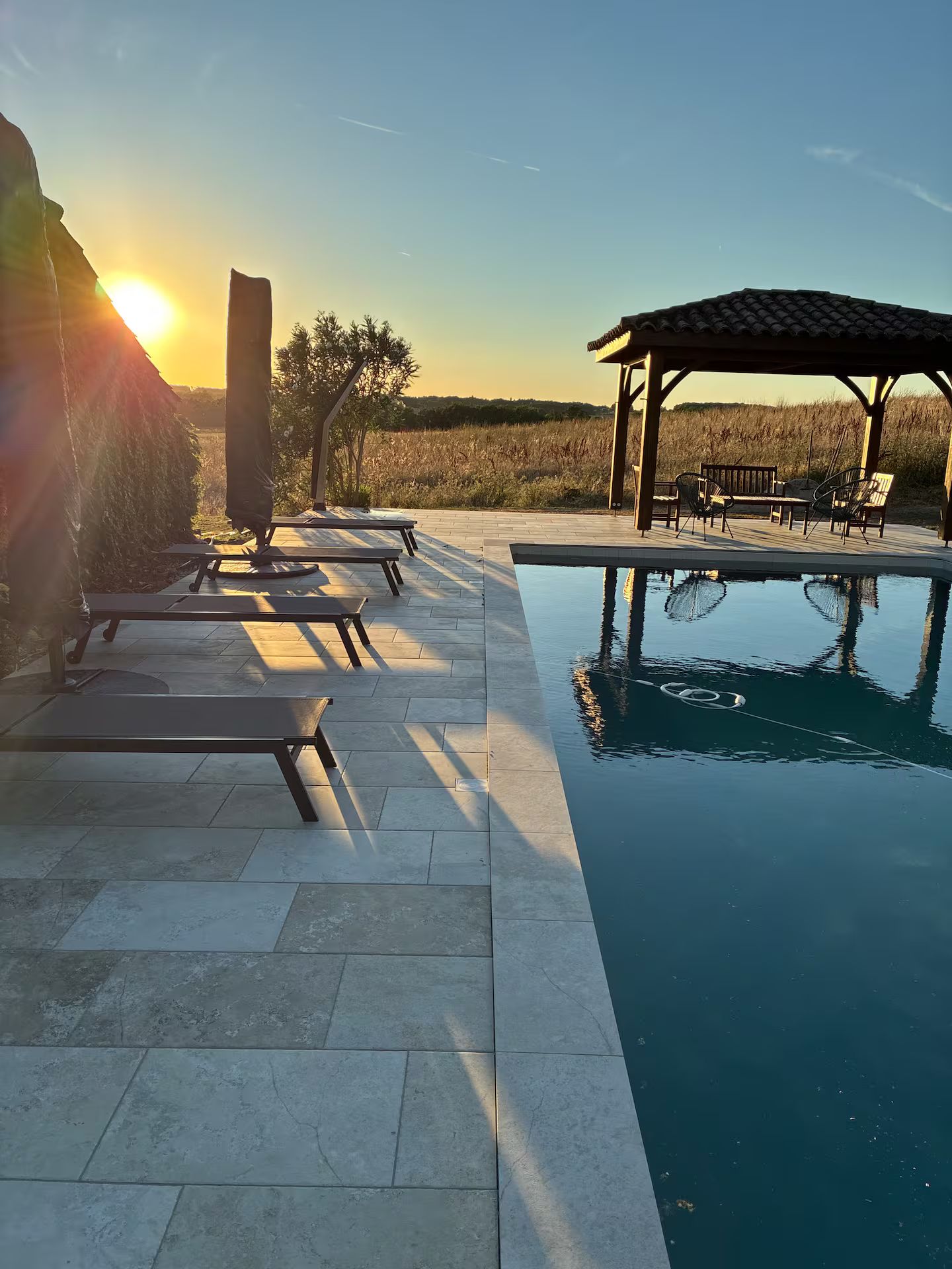 A pool area with lounge chairs and a gazebo, surrounded by a landscaped garden.