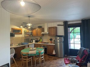 A kitchen with wooden cabinets, a stainless steel refrigerator, a dining table with chairs, and a large window with curtains. - Countryside lodge (Saint-Eutrope-de-Born)