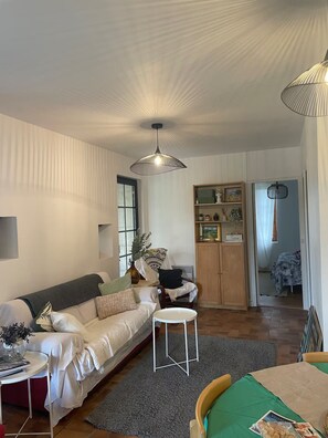 A living room with a sofa, a small table, a cabinet with decorative items, and a hanging light fixture. - Countryside lodge (Saint-Eutrope-de-Born)