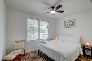 A bedroom with a bed, a nightstand, a heater, a window with blinds, a ceiling fan, and a framed picture on the wall. - Bastrop Forest Home | 3BR, Crew & Monthly Stays (Bastrop)