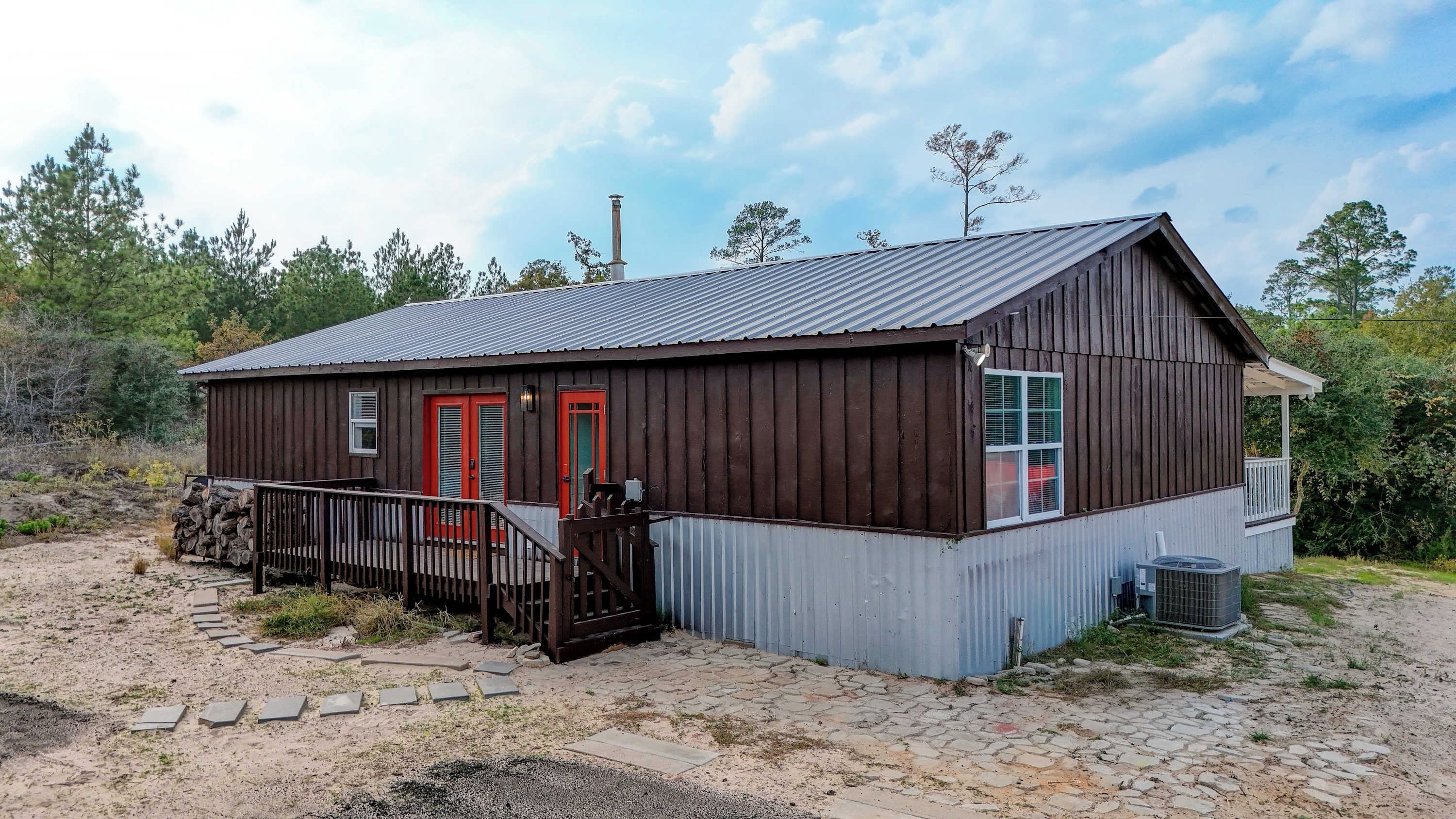 Un bâtiment rustique en bois, avec un toit en métal, une porte rouge et un petit porche.