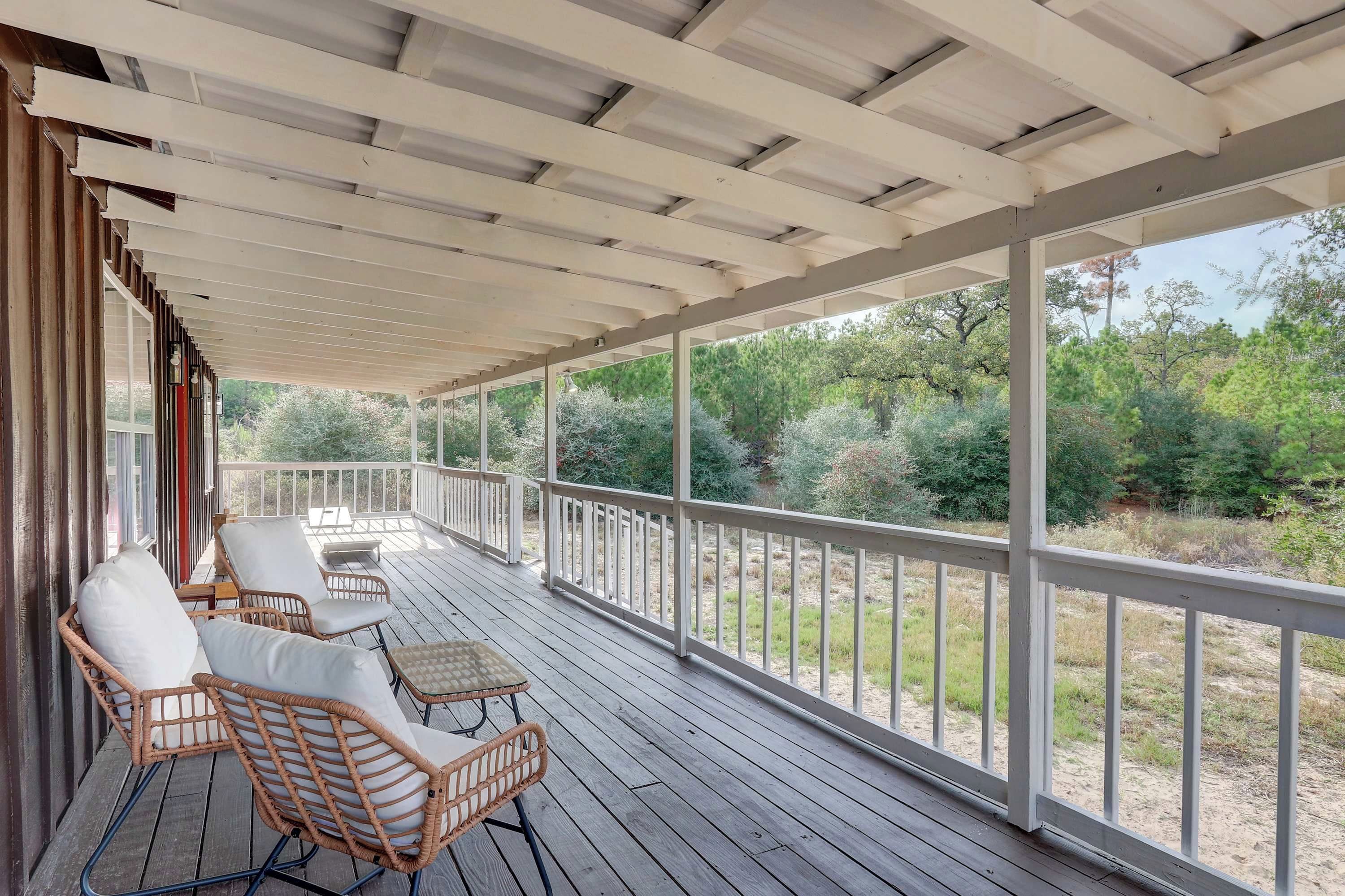 A covered outdoor deck with wicker furniture and a view of a wooded area.
