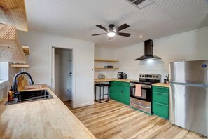 A modern kitchen with wooden flooring, a built-in oven, a stainless steel refrigerator, and a ceiling fan. - Bastrop Forest Home | 3BR, Crew & Monthly Stays (Bastrop)
