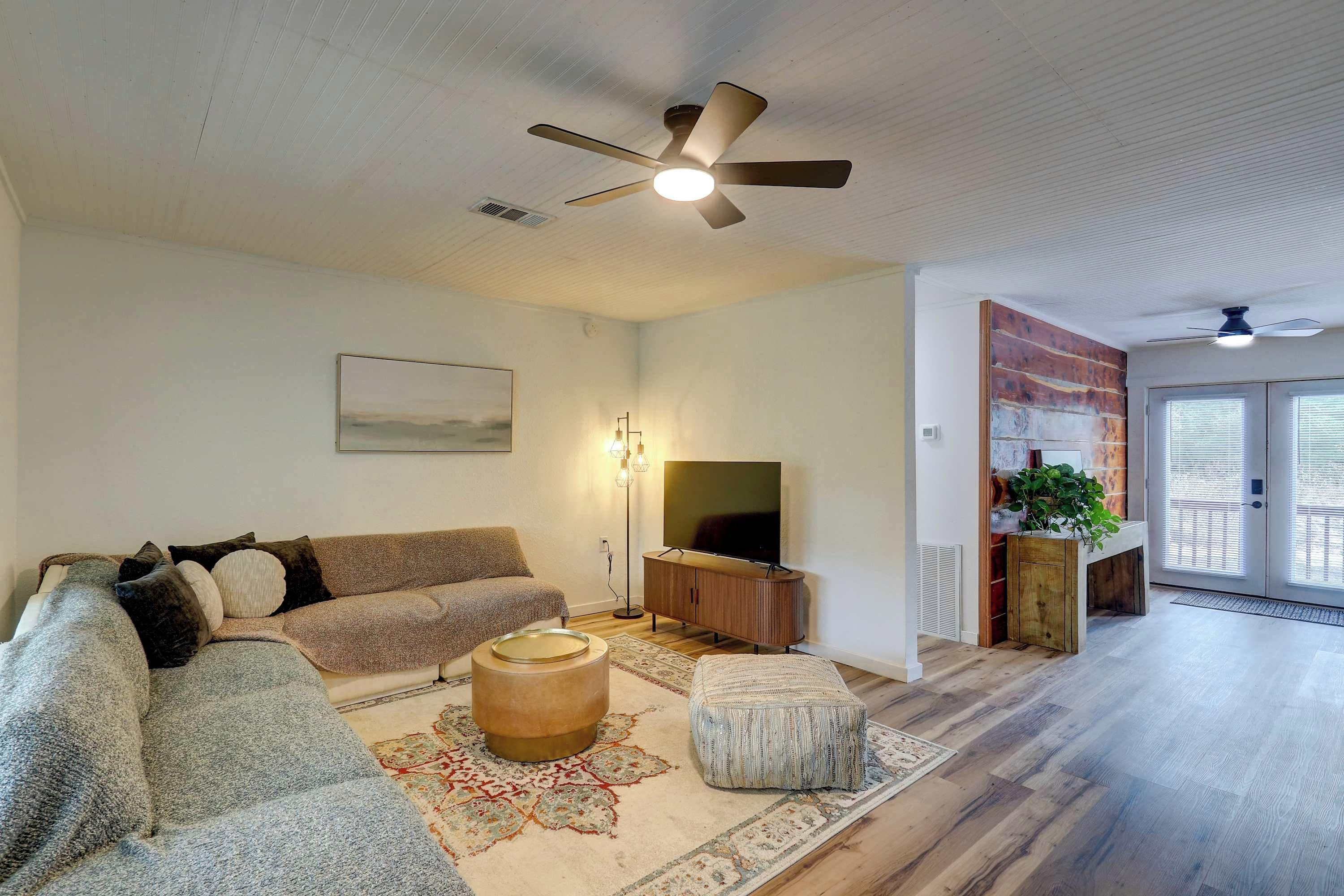 A living room with a sofa, ottoman, TV, and ceiling fan.