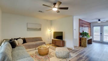 A living room with a sofa, ottoman, TV, and ceiling fan.