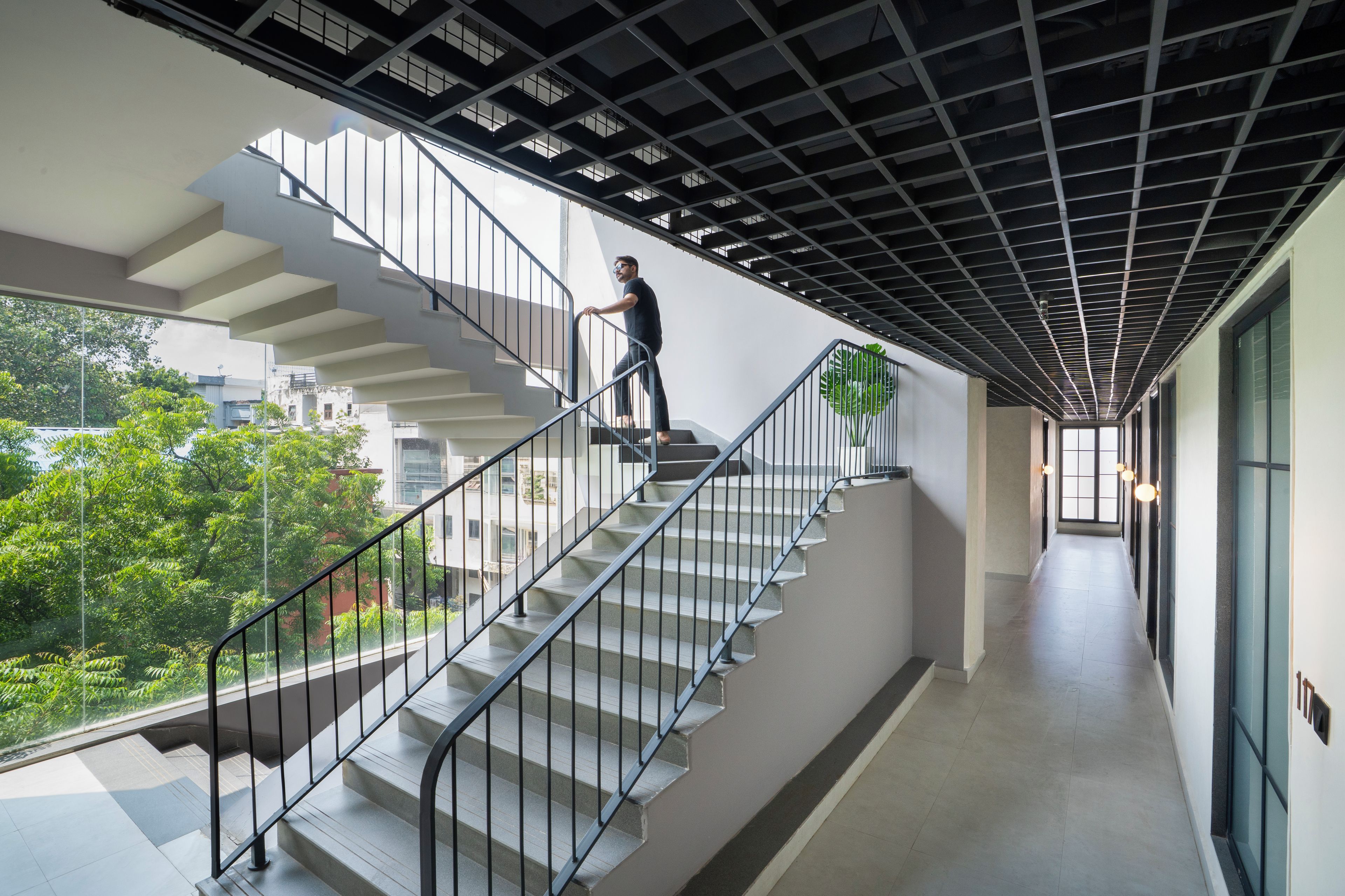 A modern staircase with metal railings and a glass balustrade, leading to a landing with a view of greenery outside.
