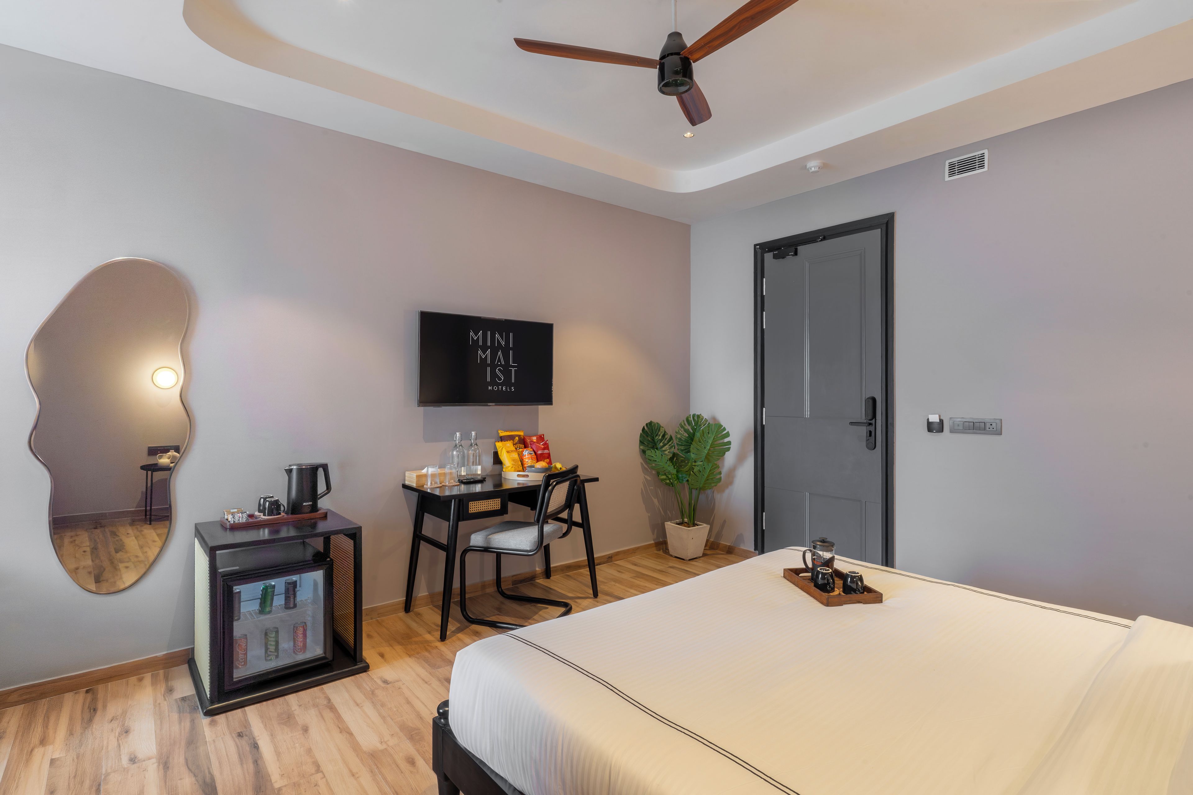 Habitación de hotel con cama, escritorio, silla, televisor, planta y minibar.