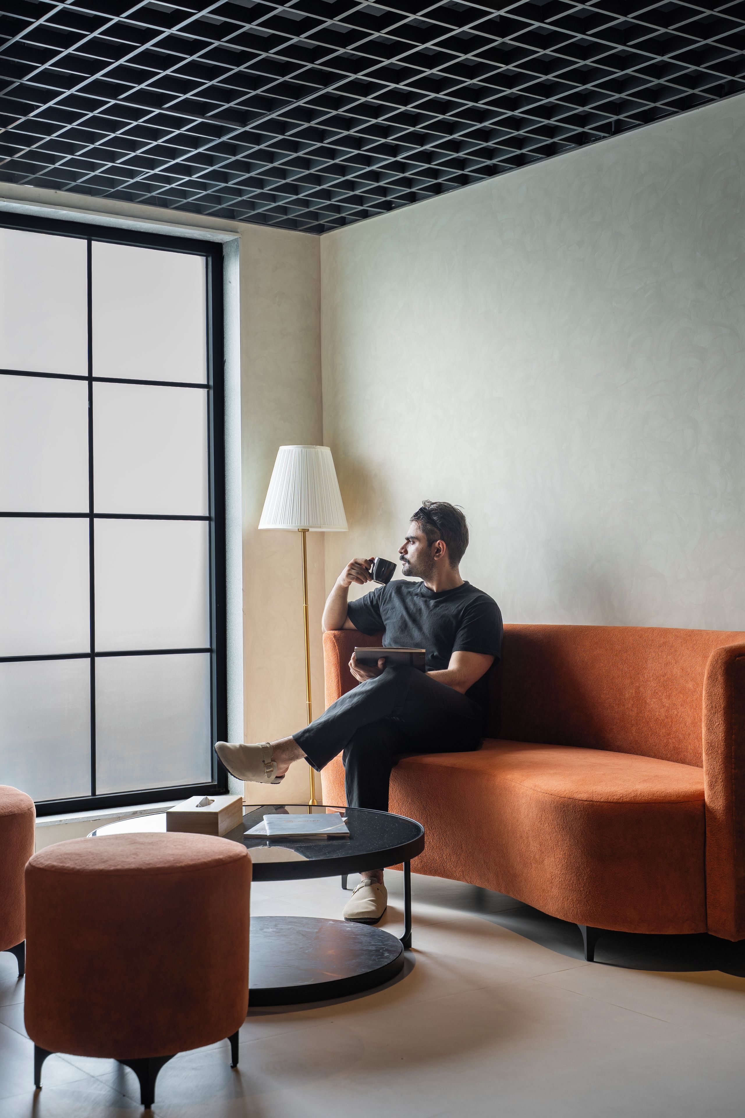 A modern interior with a person sitting on a sofa, a lamp, and a round table.