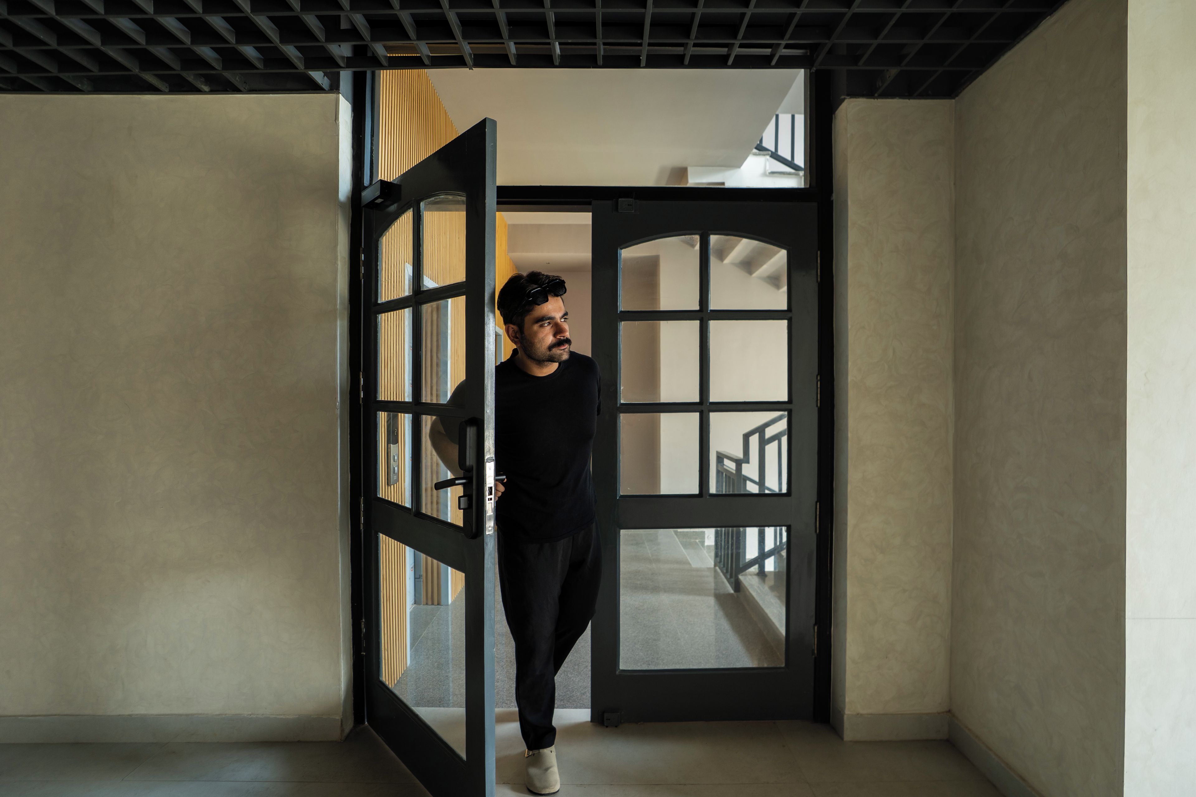A person standing in a doorway with a view of a staircase and a room with a patterned wall.