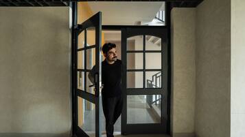 A person standing in a doorway with a view of a staircase and a room with a patterned wall.