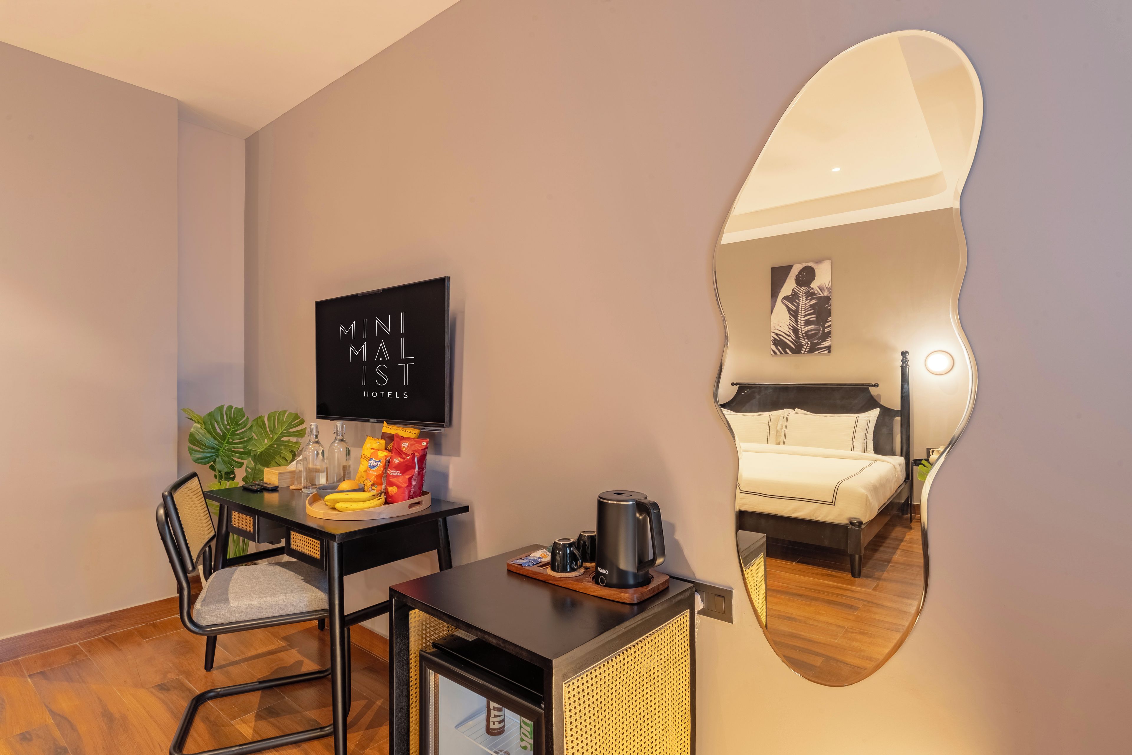 A hotel room with a bed, a desk with a chair, a television, a mirror, and a coffee machine.