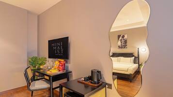 A hotel room with a bed, a desk with a chair, a television, a mirror, and a coffee machine.
