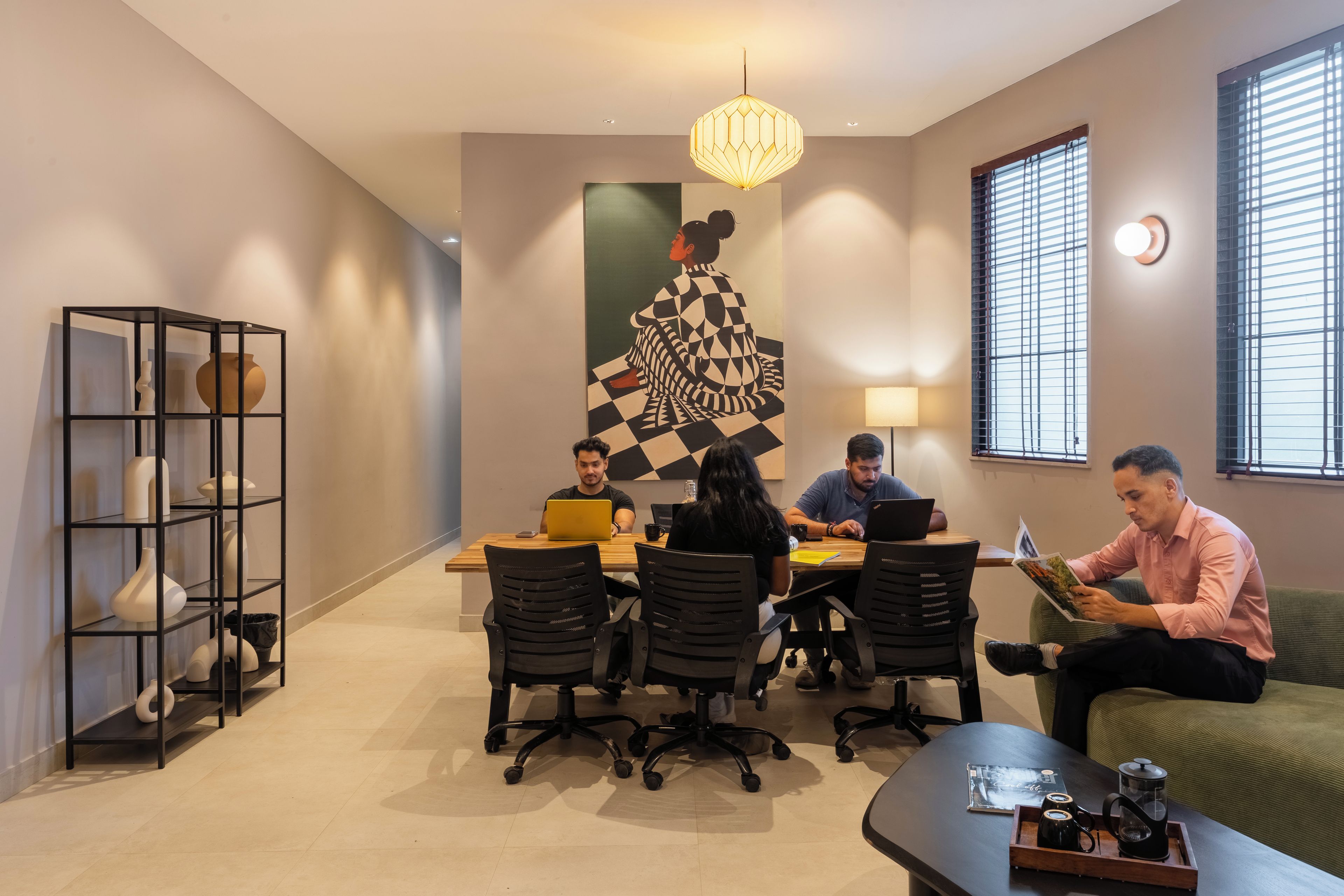 A modern meeting room with a geometric wall art, a hanging light fixture, and a coffee table with a tray.