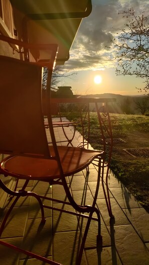 Eine Terrasse mit Tisch und Stühlen mit Blick auf eine Rasenfläche und einen Sonnenuntergang.