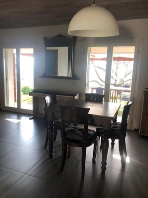 Ein Essbereich mit Tisch und Stühlen, einer großen Pendelleuchte und Blick durch Glastüren nach draußen.